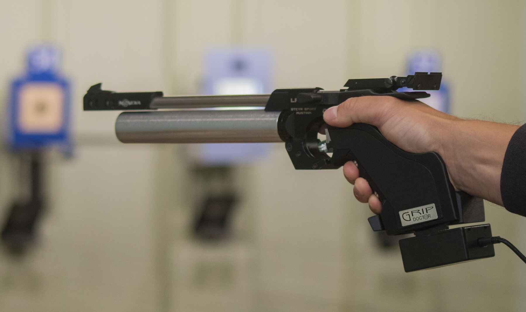 A shooter's hand on a GripDoctor-equipped competition pistol grip on the firing line